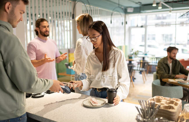Asian woman paying for coffee to go and dessert to barista via smartphone in cafe — Stock Photo