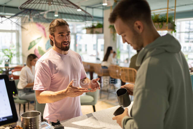 Bearded man in pink t shirt talking with male barista preparing coffee in cafe — Stock Photo