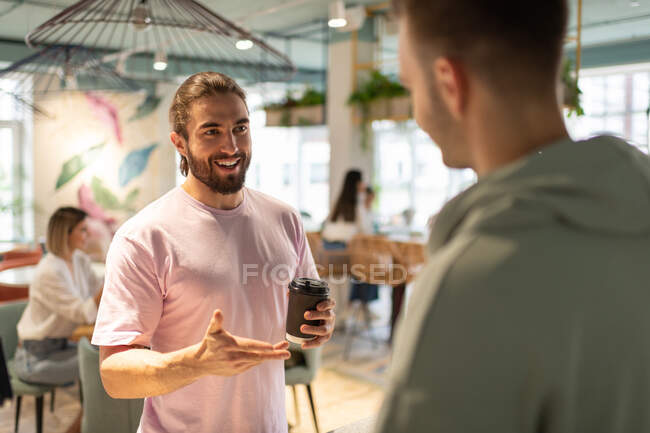 Homem feliz com café para ir sorrir e falar com barista masculino no café — Fotografia de Stock