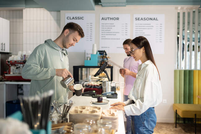 Man in casual clothes preparing coffee to go for Asian female client in cafe — Stock Photo