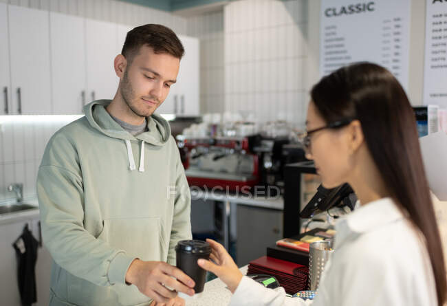 Man in casual hoodie giving beverage to go to Asian woman during work in coffee shop — Stock Photo