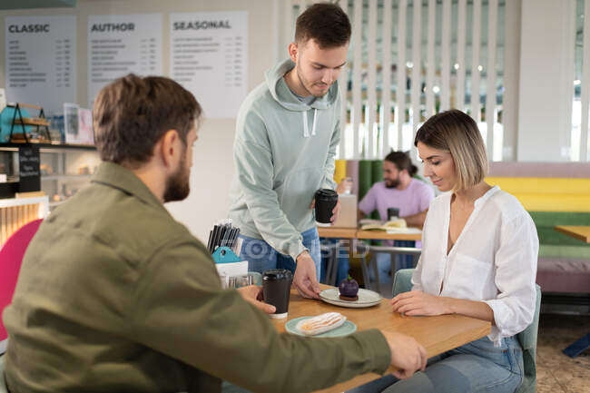 Male barista serving fresh desserts and coffee to go to man and woman in cafe — Stock Photo