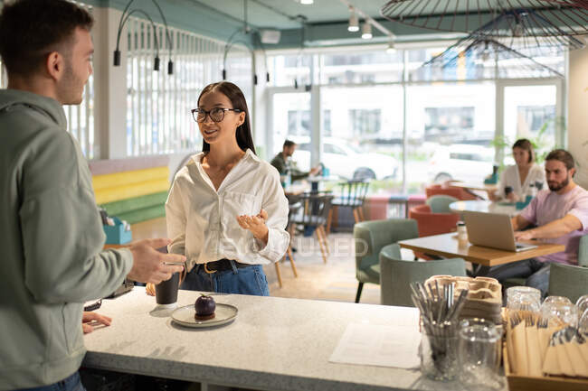 Cliente feminino sorrindo e falando com barista masculino em café moderno espaçoso — Fotografia de Stock