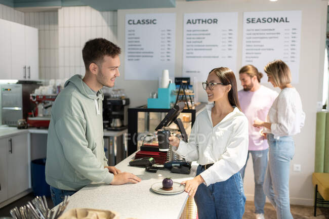 Asiatico donna con caffè e dessert sorridente e parlando con maschio barista in caffè — Foto stock
