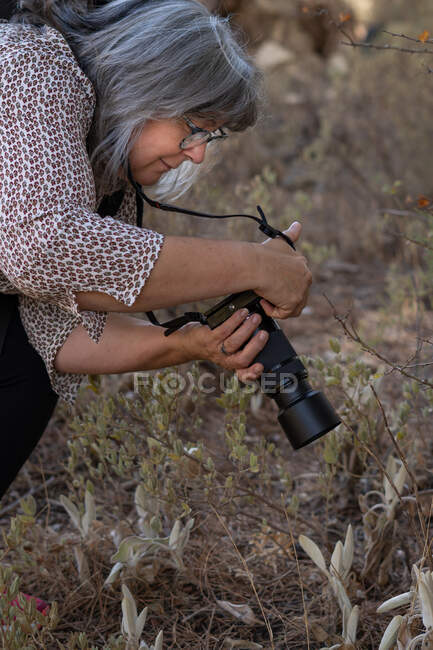 Mais velha mulher de cabelos brancos tirando fotos na floresta — Fotografia de Stock