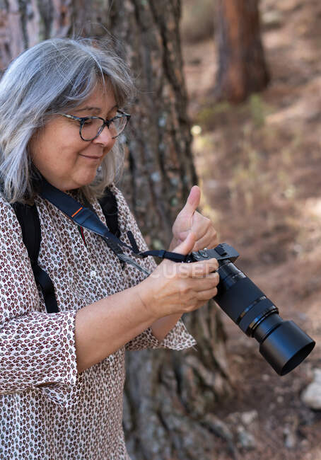 Mujer mayor de pelo blanco tomando fotos en el bosque - foto de stock