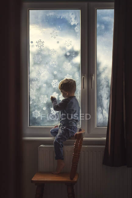 Menino pequeno em roupas azuis sentado na soleira da janela e anexando c — Fotografia de Stock