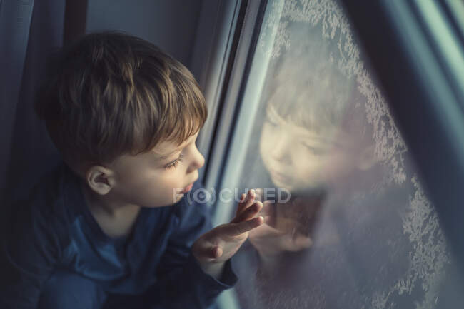 Small boy looking on frozen window and seeing his own reflection — Stock Photo