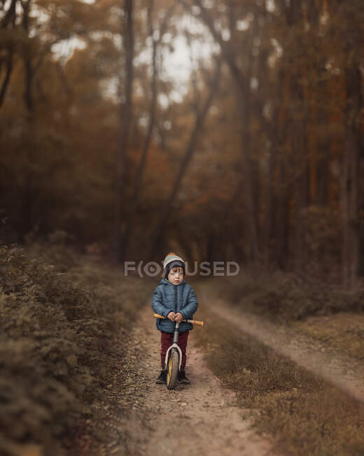 Piccolo ragazzo in giacca blu e cappello su pushbike in piedi in campagna — Foto stock