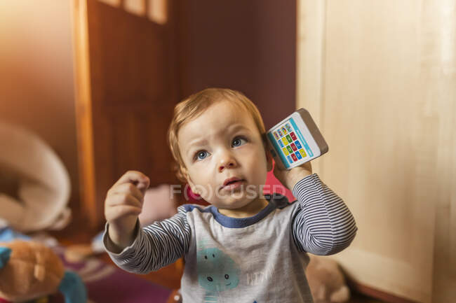 Menino pequeno que conta no telefone móvel do brinquedo ao sentar-se no f — Fotografia de Stock