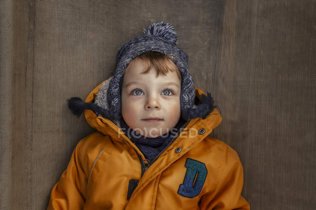 Портрет маленького мальчика в зимней куртке и теплой шляпе лежащей — стоковое фото