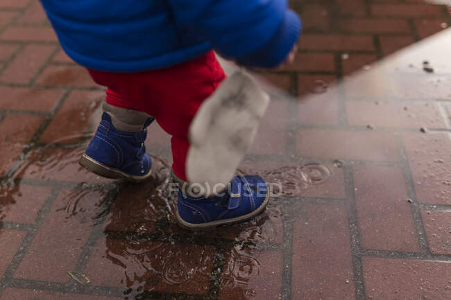 Bassa sezione di bambino che cammina in pozzanghera all'esterno — Foto stock