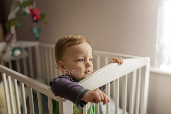 Small blonde boy standing in his crib — Stock Photo