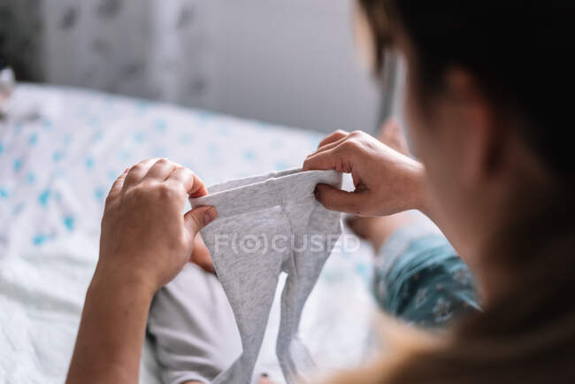 Madre vistiendo a su bebé en la cama. Poniéndose los pantalones. - foto de stock