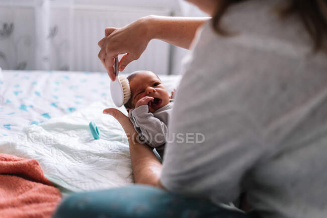 Mãe penteando o cabelo de seu bebê na cama. — Fotografia de Stock