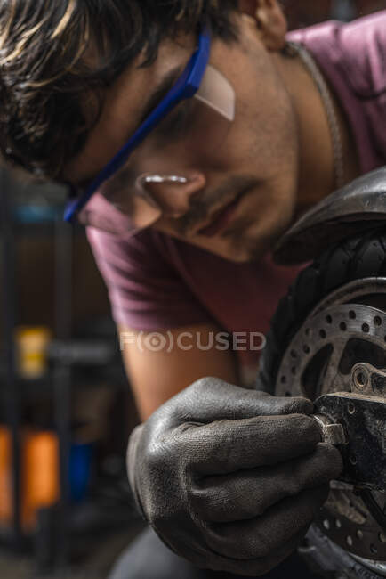 Immagine verticale di un meccanico con occhiali di sicurezza che mette in atto la ruota di uno scooter elettrico con i relativi bulloni o dadi in officina. — Foto stock