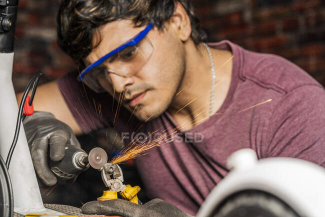 Um mecânico focado usando óculos de segurança usando um mini moedor para cortar um parafuso na reparação de uma scooter elétrica. — Fotografia de Stock