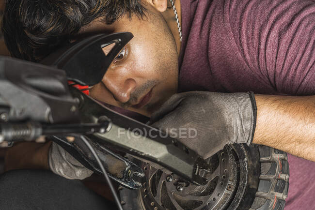 Primer plano de un joven mecánico latino comprobando cuidadosamente el cableado que va al volante de un scooter eléctrico en su taller - foto de stock