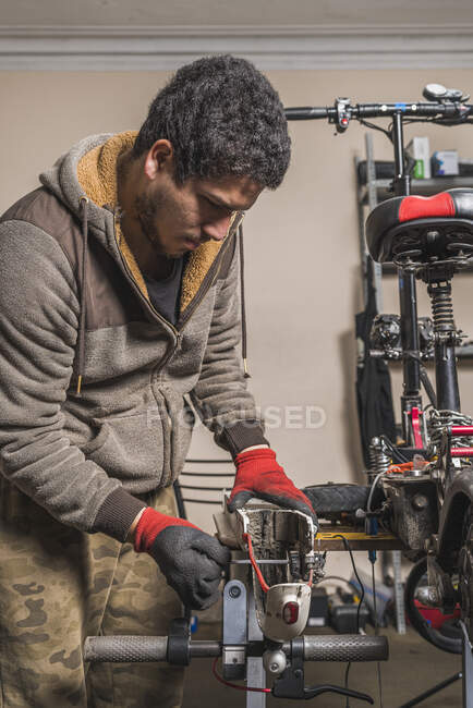 Image verticale d'un mécanicien réparant une aile d'un scooter électrique sur une table dans l'atelier. — Photo de stock