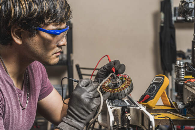 Seitenansicht eines Spezialisten mit digitalem Multimeter zur Überprüfung der korrekten Spannung eines Elektrorollers in einer Fachwerkstatt. — Stockfoto