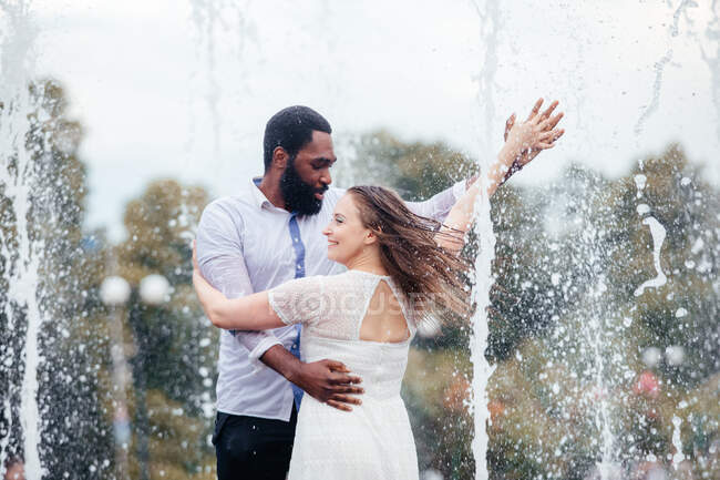 Das schöne junge Paar aus unterschiedlichen Menschen tanzt gemeinsam in einem Stadtbrunnen — Stockfoto
