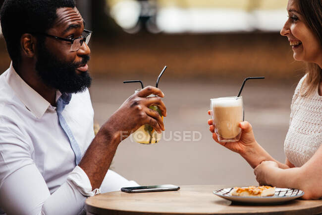 The happy young couple of diverse people are drinking and spent nice time in a street cafe — Stock Photo