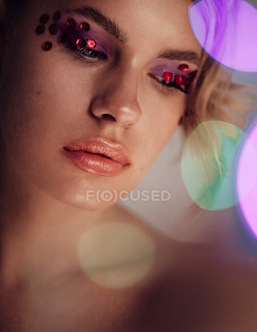 Fashion Beauty Girl Portrait Isolated on golden Christmas glittering bokeh lights background. Glamour Makeup. Gold Jewelry. Hairstyle. Alluring brunette with sensual red lipstick looking at camera. — Stock Photo