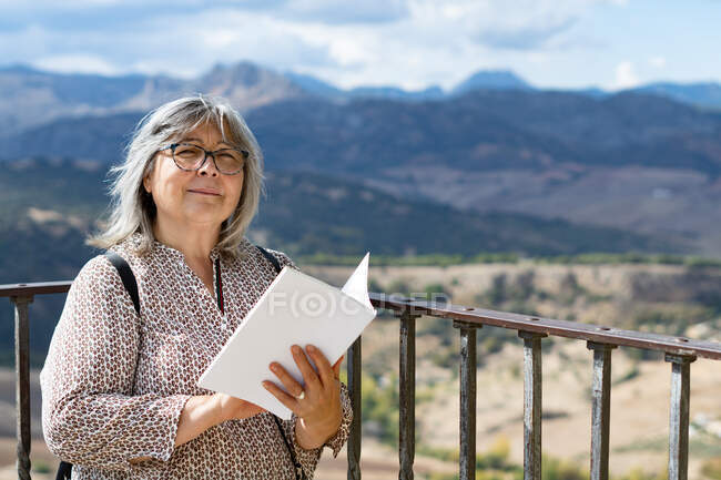 Donna dai capelli bianchi con gli occhiali che legge un libro nel parco — Foto stock