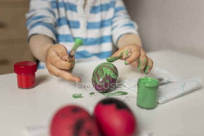 Schmutzige Hände eines Jungen, der zu Hause Osterei mit grüner Farbe bemalt — Stockfoto