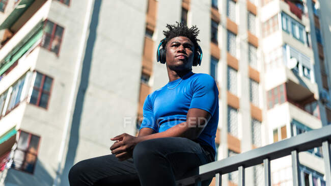 Junger schwarzer Mann hört Musik mit Kopfhörern. Turm der Wohnungen Hintergrund. — Stockfoto