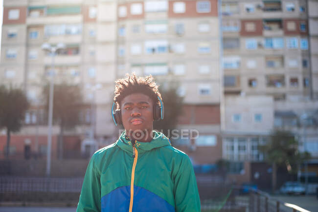 Hombre afroamericano negro escuchando música con auriculares. Fondo apartamentos residenciales. - foto de stock