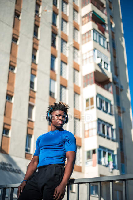 Athletic black male athlete listening to music in the city. Tower of apartments background. — Stock Photo