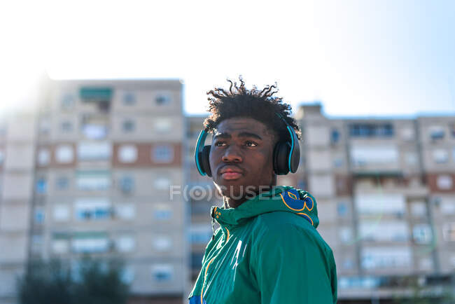 Hombre afroamericano negro escuchando música con auriculares. Vestido con una sudadera verde. - foto de stock