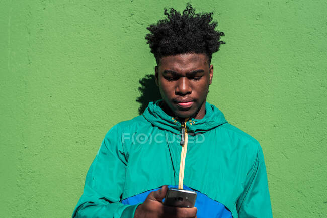 Niño negro usando su teléfono móvil. Fondo de pared verde. - foto de stock