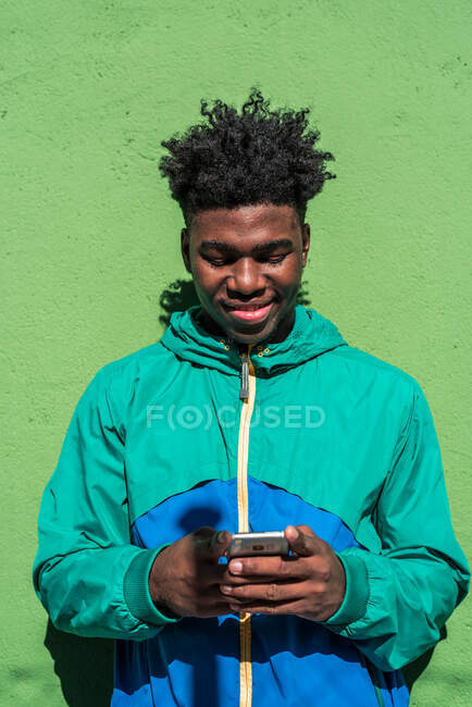 Niño negro usando su teléfono móvil. Fondo de pared verde. - foto de stock