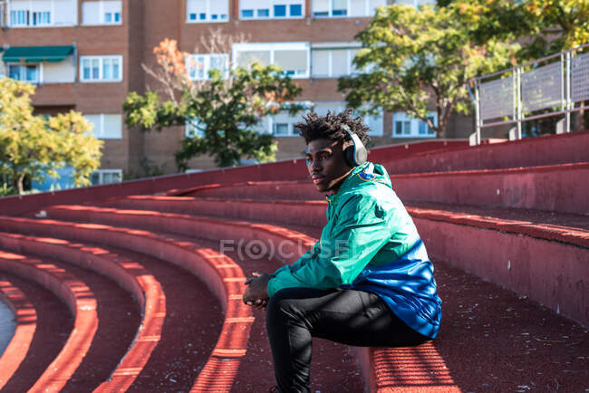 Joven hombre negro relajándose mientras escucha música en la ciudad. - foto de stock