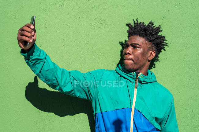 Black boy prend un selfie avec son téléphone portable. Fond de mur vert. — Photo de stock