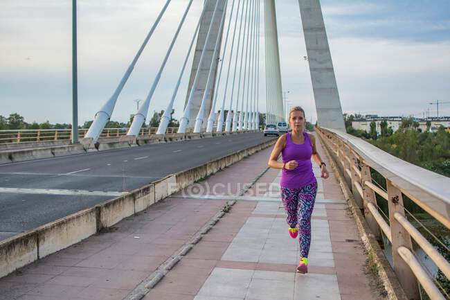 Молода жінка біжить на мосту в місті — стокове фото