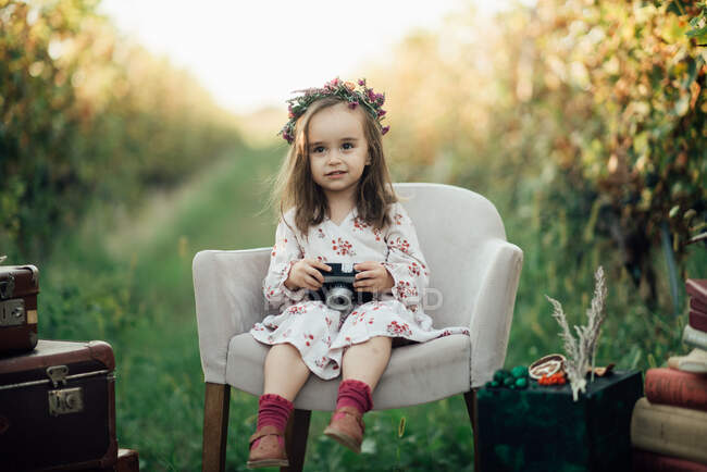 Young girl sitting on an armchair in a vineyard and playing with — Stock Photo