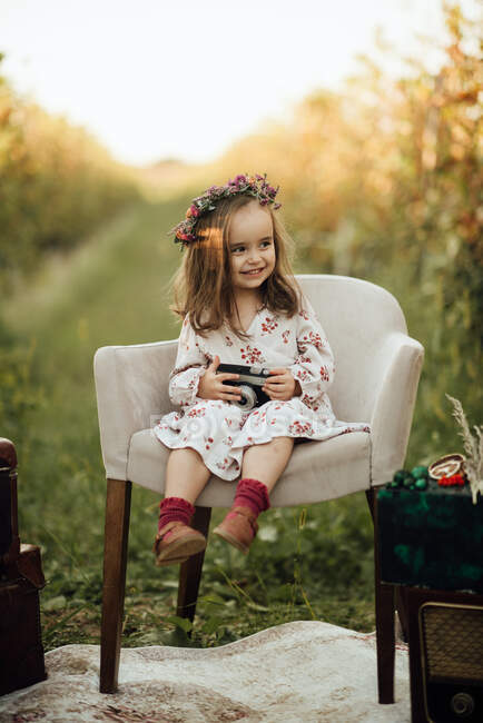 Chica feliz sentada en un sillón en un viñedo y sosteniendo una ca - foto de stock
