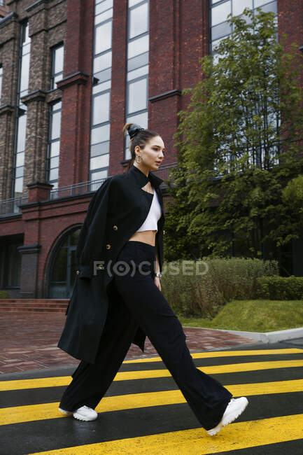 Junge schöne Frau in einem schwarzen Kleid und einer Jacke auf einer Straße — Stockfoto