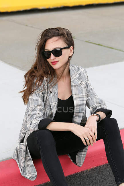 Young woman in sunglasses and jacket sitting on the street — Stock Photo