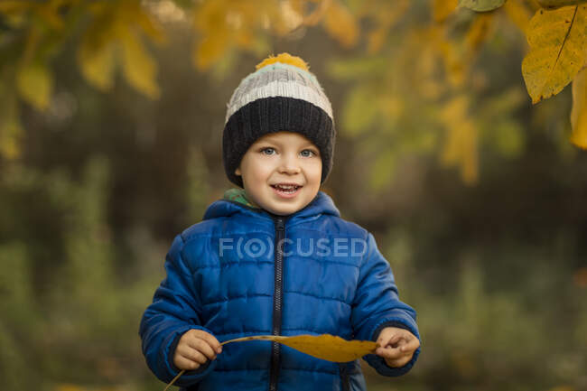 Portrait of a small boy in garden in blue jacket holding a yello — Stock Photo