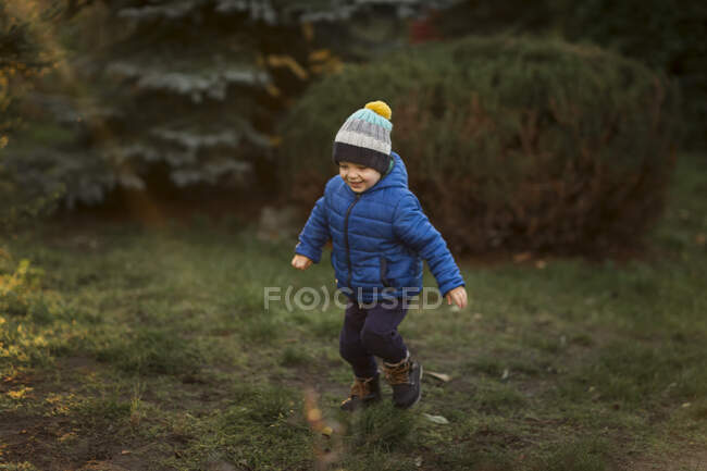 Мальчик бегает в саду во время заката в синей куртке — стоковое фото