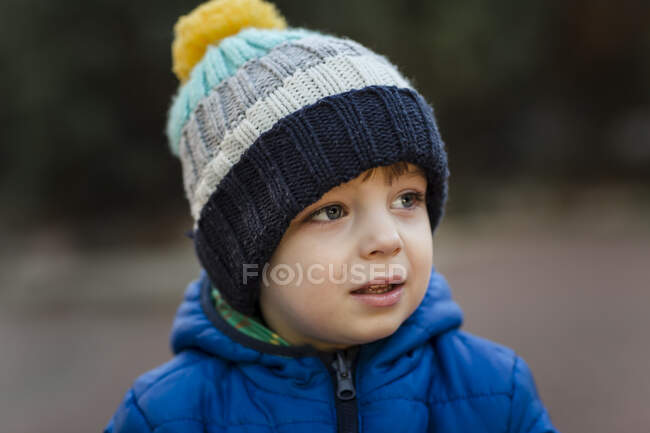 Portrait of small boy in garden in blue jacket and warm hat — Stock Photo