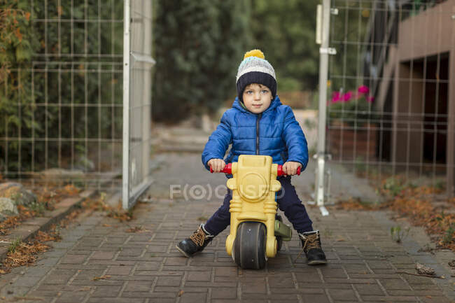 Мальчик на пластиковом игрушечном мотоцикле в саду — стоковое фото