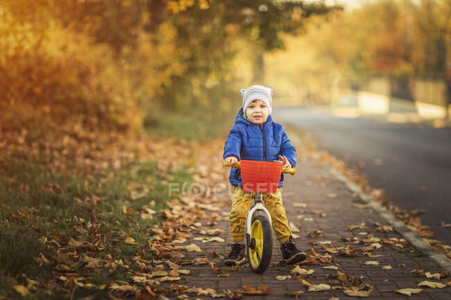 Little boy in blue jacket and yellow trousers sitting on push bi — Stock Photo