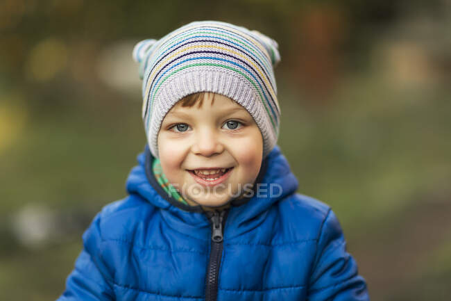 Niño pequeño con ojos azules y chaqueta azul riendo al aire libre - foto de stock