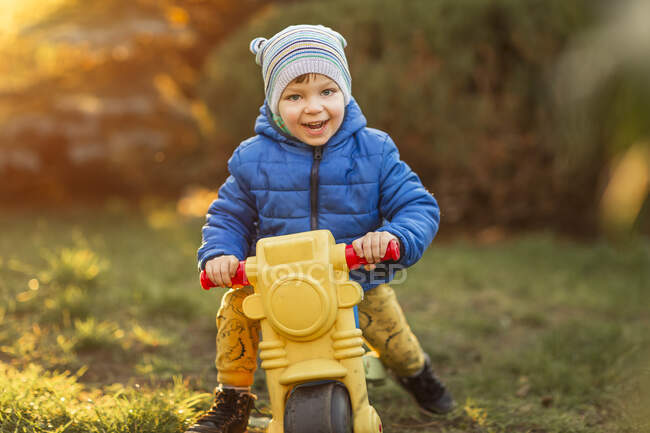 Niño pequeño con ojos azules y chaqueta azul sentado en juguete de plástico - foto de stock