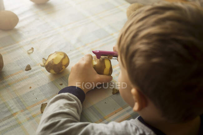 Bonito poy pilling potatoe em casa — Fotografia de Stock